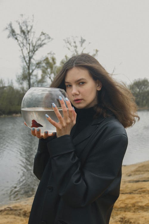 Free Woman in Black Coat Holding a Fish Bowl with Betta Fish Stock Photo