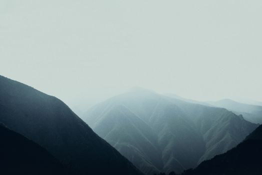 Foggy mountain landscape with eroded peaks under an overcast sky, creating a serene nature scene.