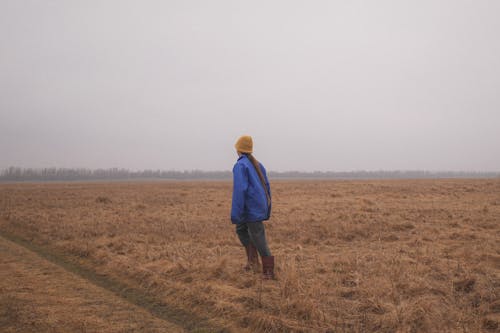 A Person in Blue Jacket Standing on Brown Field