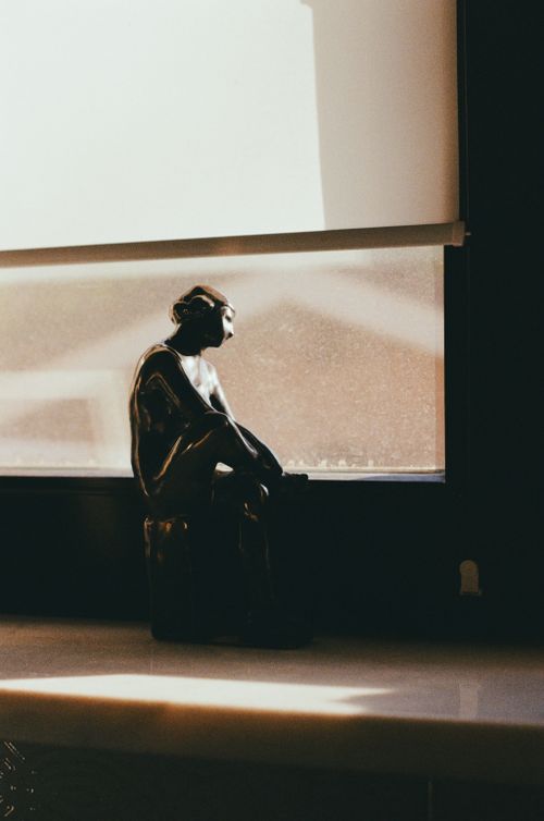 Free Bronze sculpture of a figure in silhouette on a sunlit windowsill, creating an introspective mood. Stock Photo