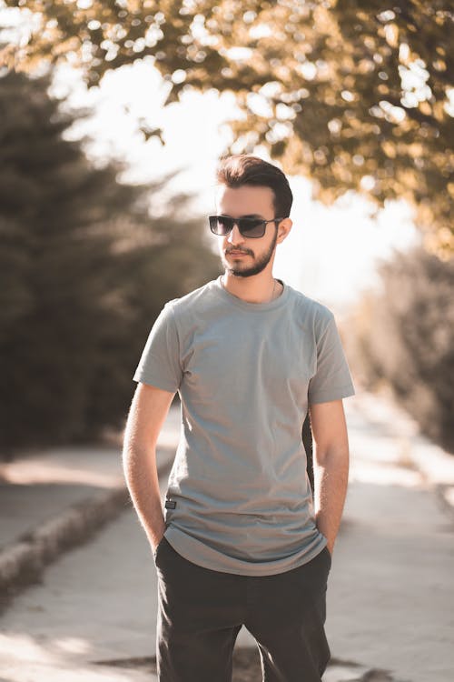 A Man in Gray Shirt Wearing Black Sunglasses Standing on the Street while  His Hands is in the Pocket of His Pants · Free Stock Photo