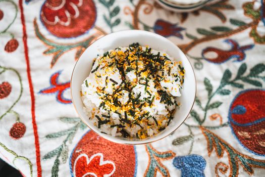 Delicious bowl of seasoned rice topped with seaweed on colorful, embroidered cloth.