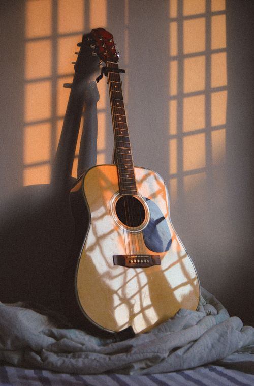 Free Sunlit acoustic guitar with shadow patterns on a cozy bed setting. Stock Photo