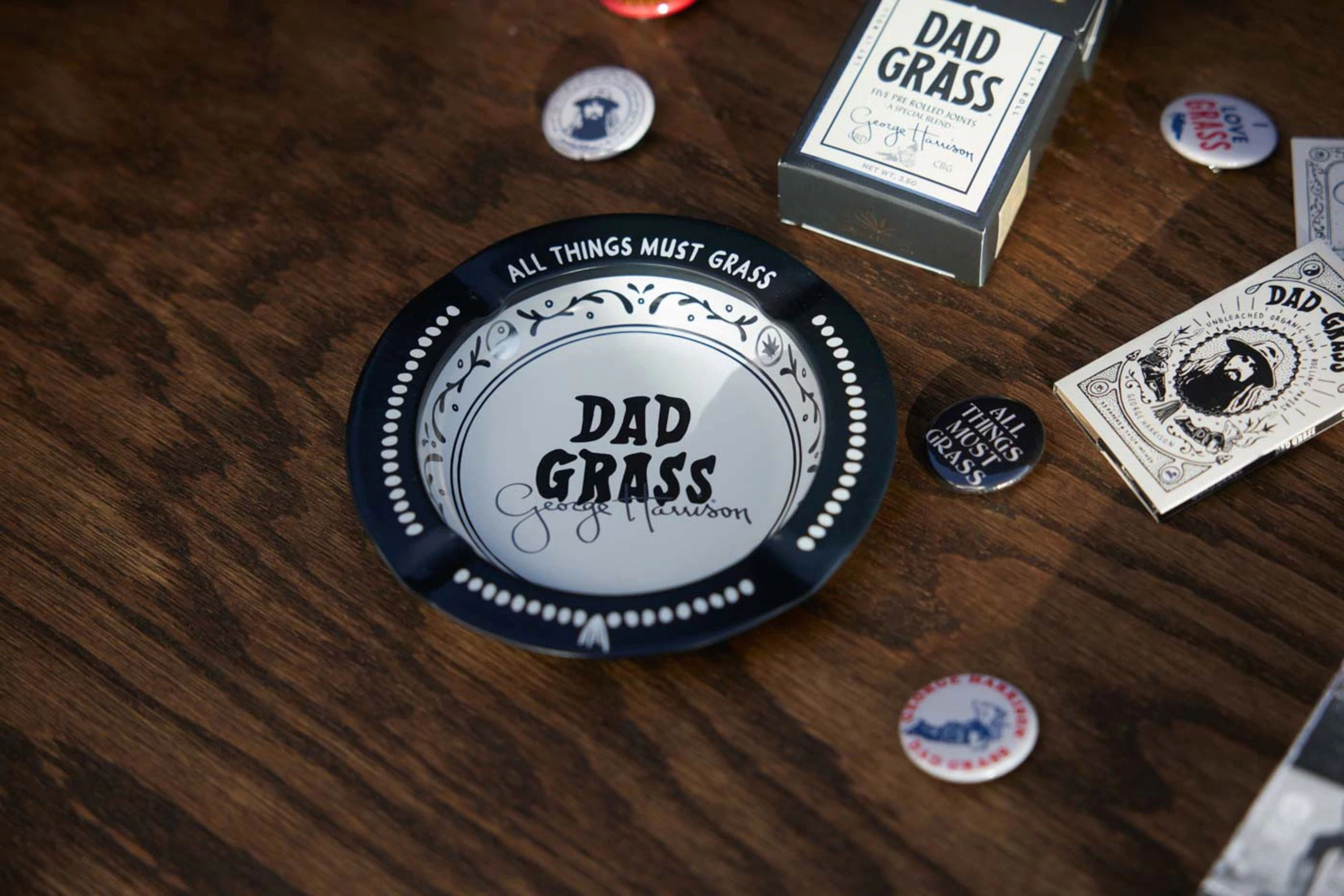 A close-up of a Dad Grass ashtray and related items on a wooden surface.