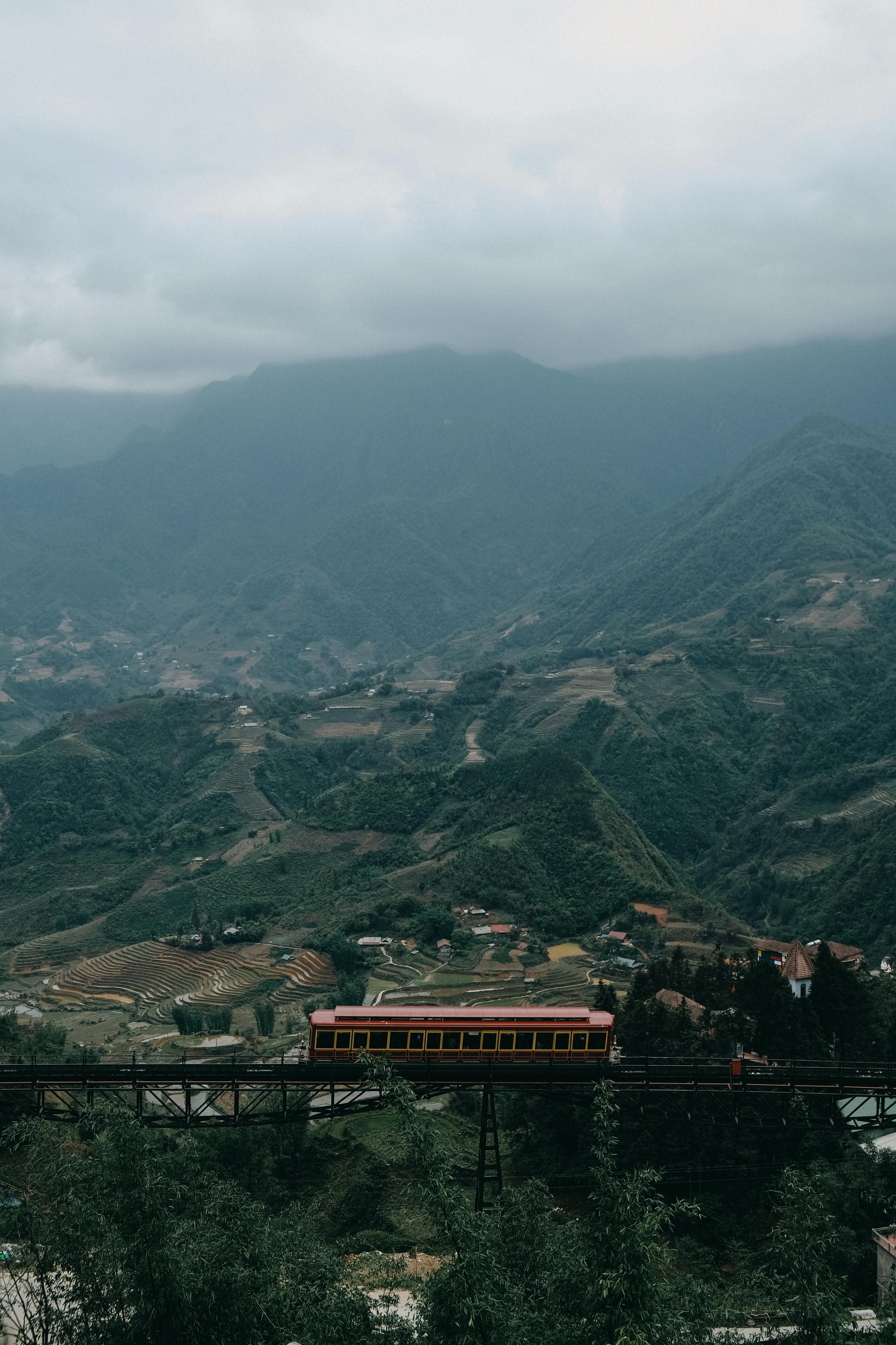 A picturesque railway bridge passes over lush valleys under an overcast sky.