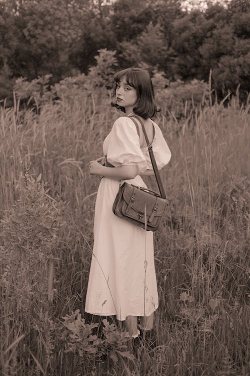 Woman in Dress and Shoulder Bag Standing on Grass Field