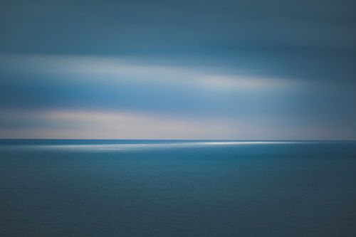 Free A serene ocean view with a dramatic moody sky and subtle light reflections on the water. Stock Photo
