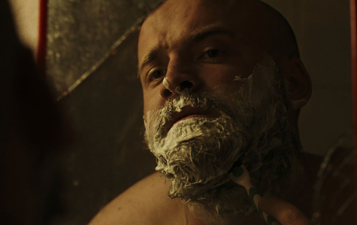 Man shaving his beard while looking in a mirror