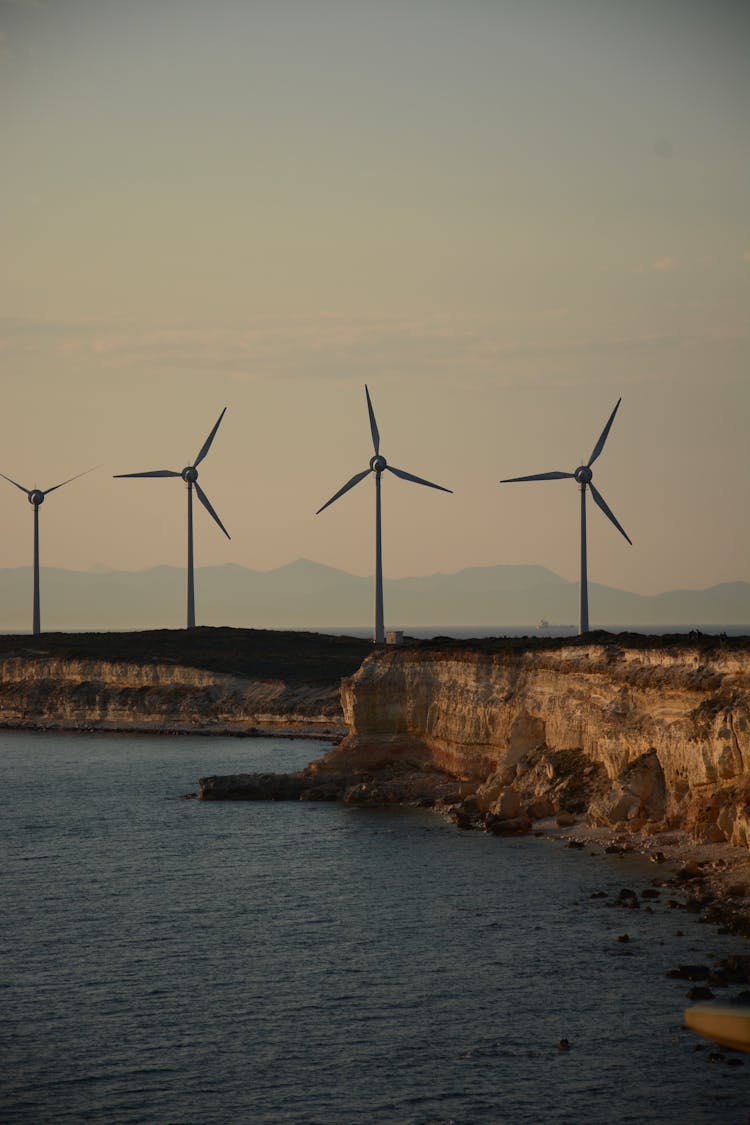 Windmills On Rocky Coastline Near Ocean