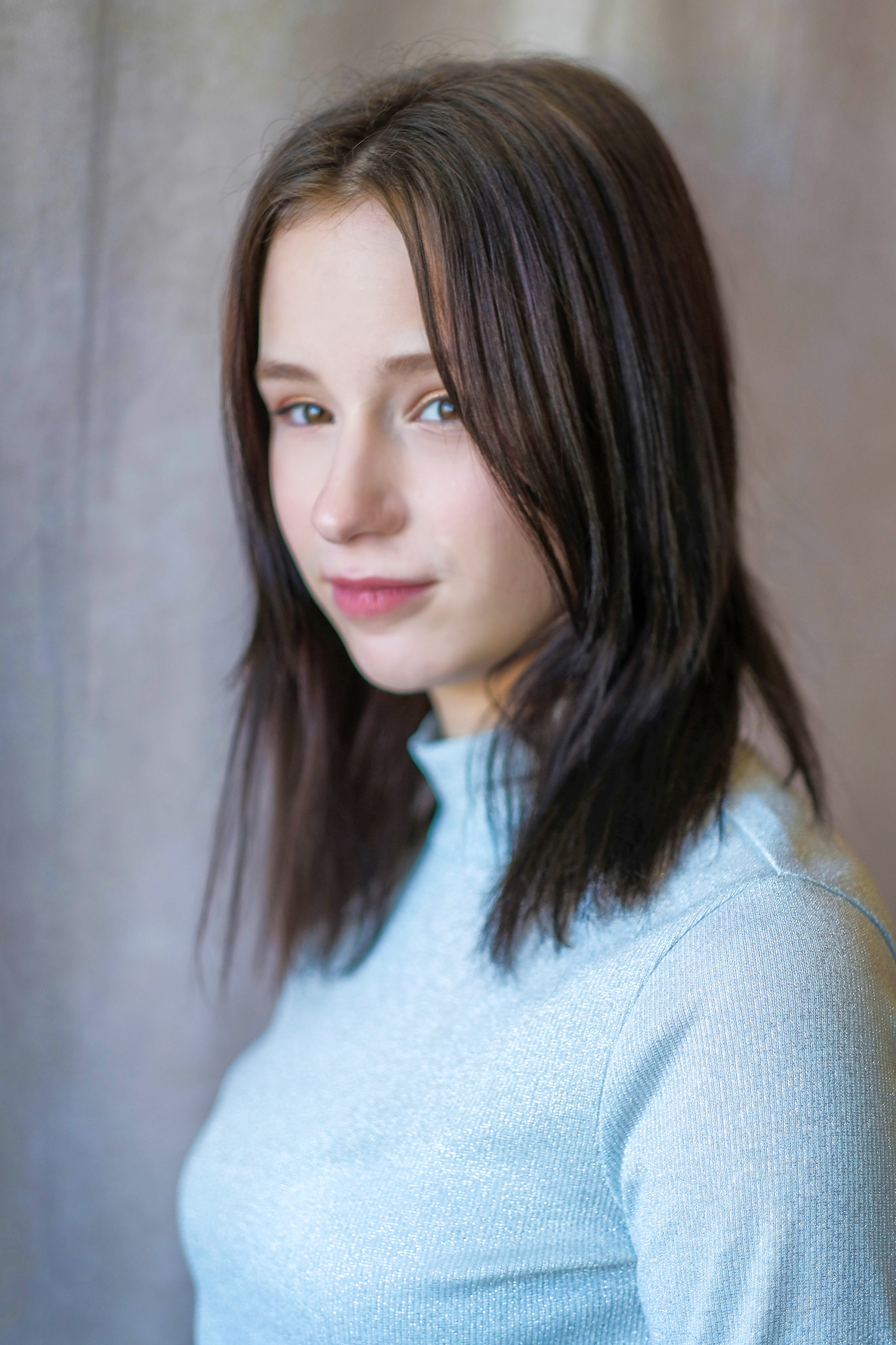 A striking portrait featuring a young woman in a light blue sweater with soft background tones.