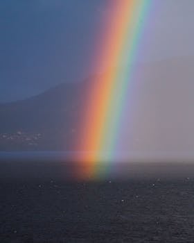 Stunning rainbow arches over a calm Norwegian fjord during dusk.