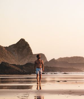 Man walking shirtless on a scenic Portuguese beach at sunset. Tranquil coastal scene.