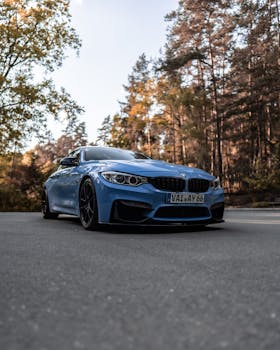 A stylish blue BMW parked on a scenic road surrounded by a lush forest under daylight.