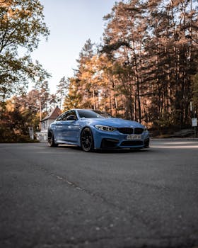 A sleek blue sedan parked on a road surrounded by lush trees during daylight.