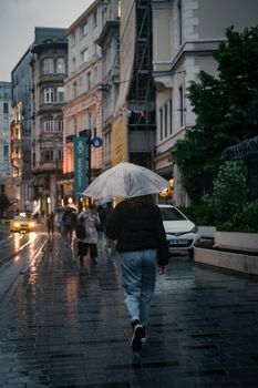 A person walking with an umbrella on a rainy city street in the evening.