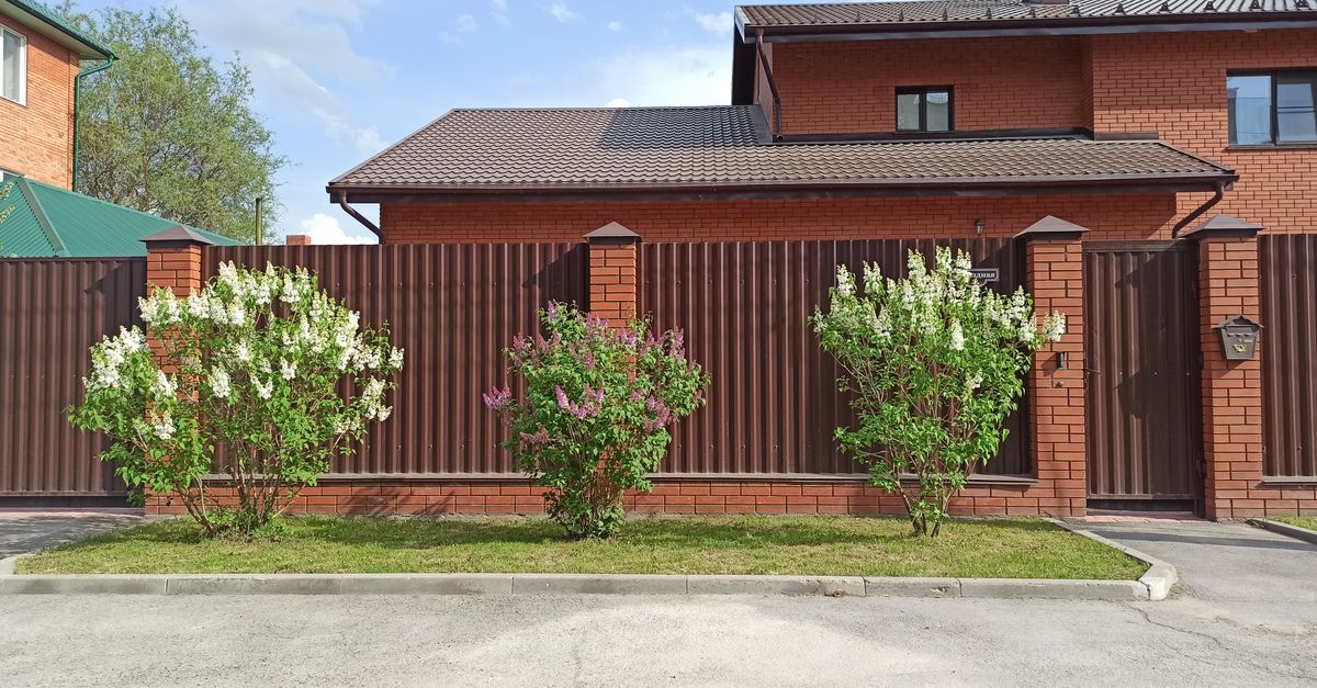 Elegant brick house with brown metal fence and flowering bushes in Berdsk, Russia