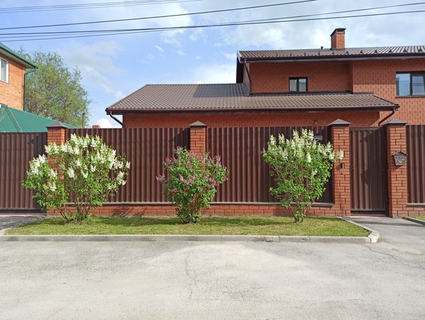 Elegant modern metal fence in front of a brick house with garden
