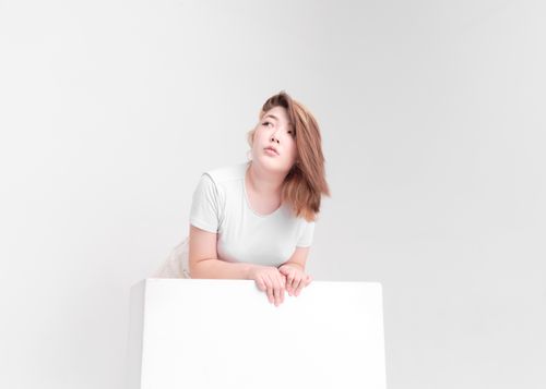 Free Studio portrait of a woman leaning on a white block, looking upwards with a contemplative expression. Stock Photo