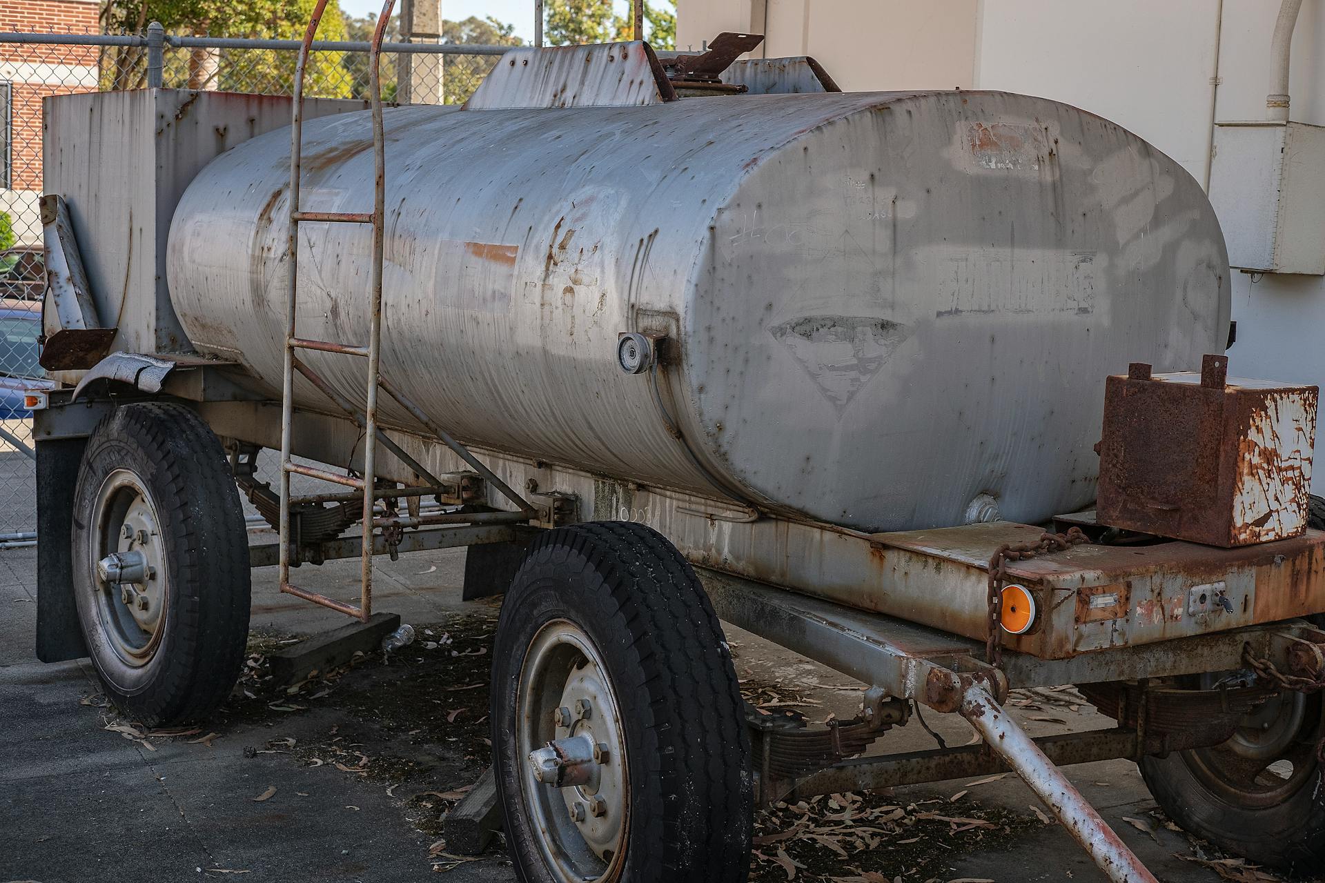 Close-up of a rusty, abandoned water tank trailer with wheels and ladder outdoors.