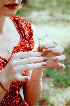 Close-up of a woman holding white daisies with manicured hands, wearing a red floral dress.