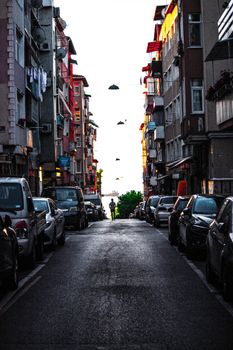 A narrow street in İstanbul lined with parked cars and tall buildings during twilight.