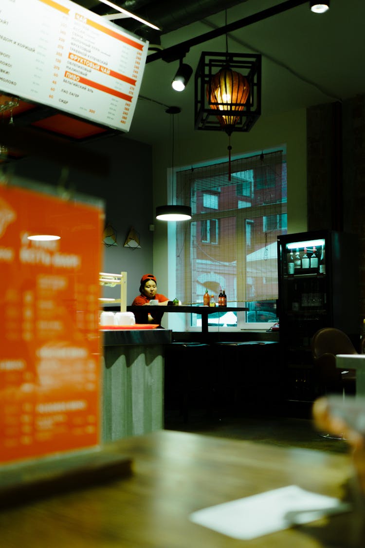 Young Woman Waitress Sitting Alone Behind Counter At Cafeteria