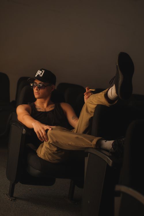 Free Young man in a black tank top and cap relaxing in a dark room with dim lighting. Stock Photo