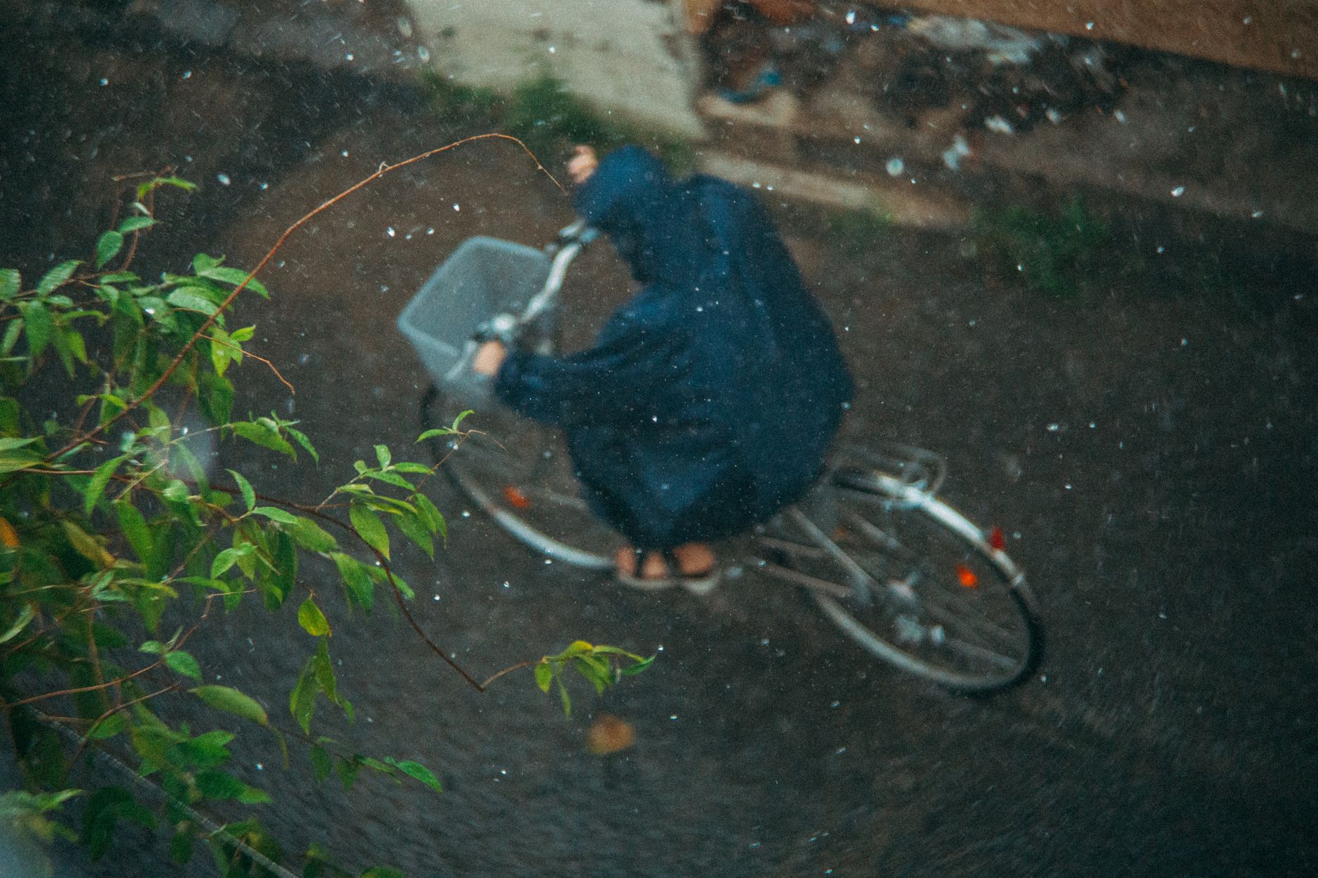 Cyclist in a rain jacket riding a commuter bike on a wet road during a rainstorm