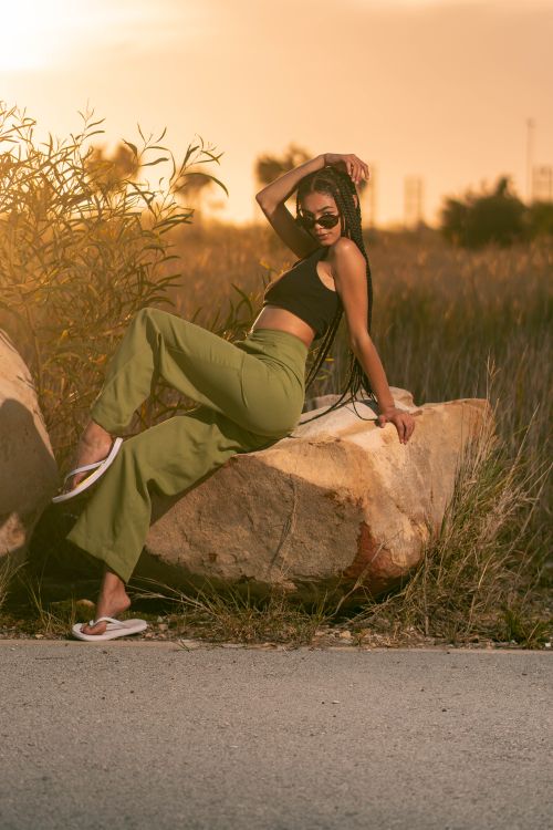 Free Stylish African American woman posing on rock in vibrant outdoor setting, showcasing modern fashion. Stock Photo