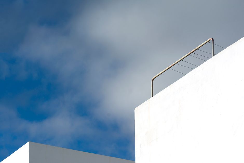 A minimalist view of white architecture with a railing against a bright cloudy sky.