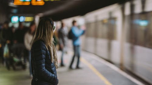 Woman in Black Winter Clothing Standing on a Platform Near Moving Train