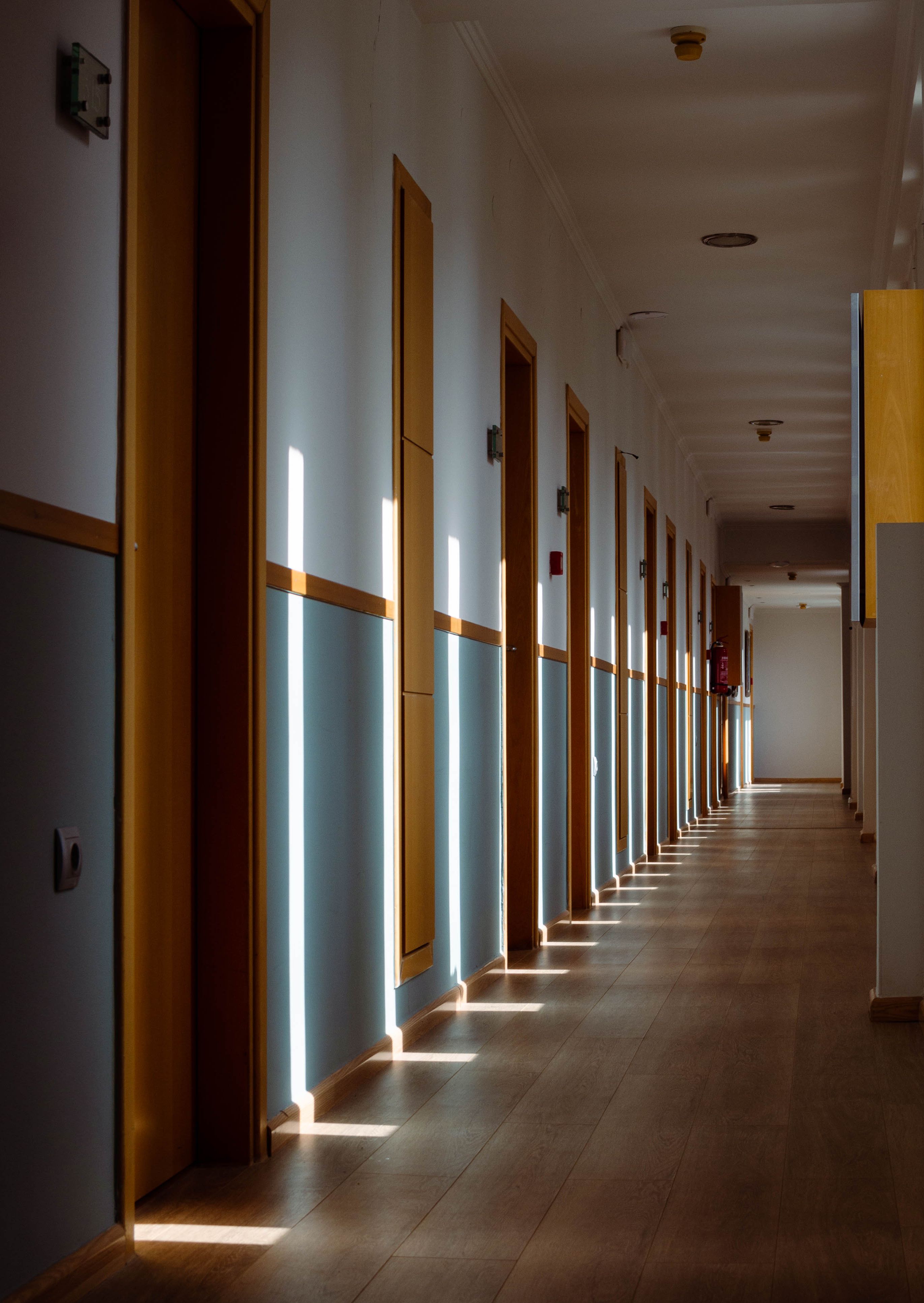 A narrow hallway with wooden doors and sunlight creating patterns on the floor in Kalamata, Greece.
