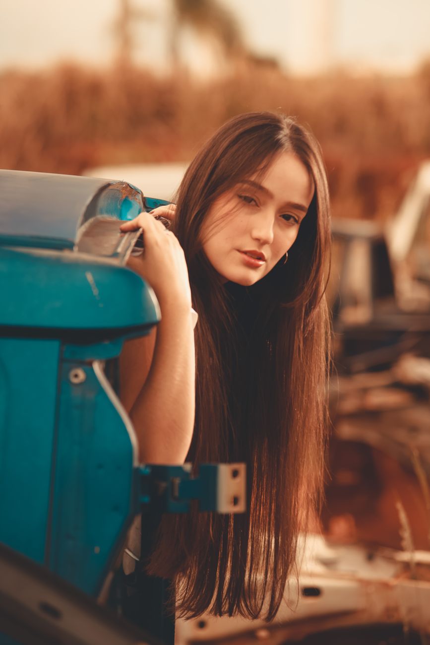 Stylish portrait of a young woman leaning on a car in a vintage setting. Warm tones and timeless appeal.