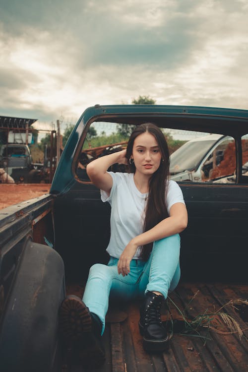 Free Woman in White Shirt and Blue Denim Jeans Sitting on Black Car Stock Photo