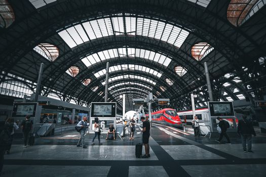 Commuters at Milano Central Station featuring modern trains under the iconic arched roof.