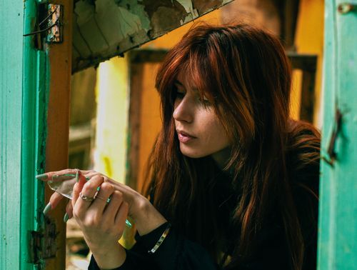 Free A thoughtful woman with red hair holds broken glass in an abandoned building interior. Stock Photo