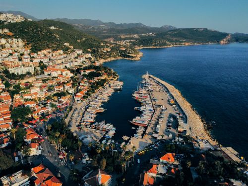 Free Stunning aerial view of a vibrant coastal town with a busy harbor, surrounded by lush hills and deep blue sea. Stock Photo