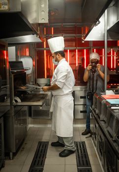 Chef cooks while photographer captures the process in a professional kitchen.