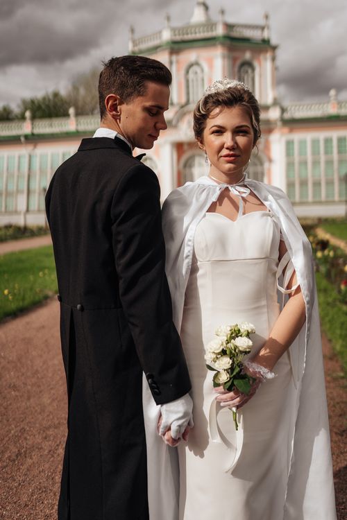 Free A stylish couple in wedding attire posing outdoors in front of a historic building. Stock Photo