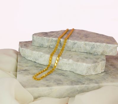 Close-up of a gold necklace elegantly displayed on marble stones, perfect for showcasing luxury jewelry.