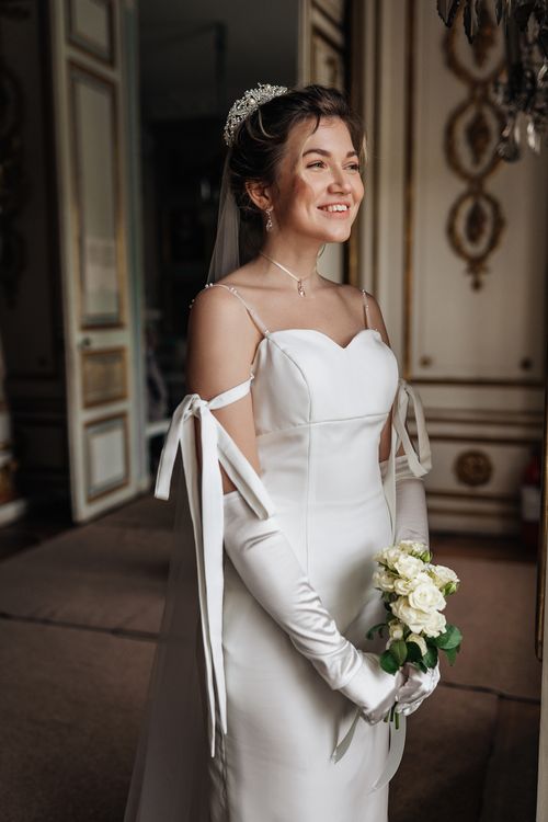 Free A bride in a classic wedding dress stands indoors holding a bouquet, radiating happiness. Stock Photo