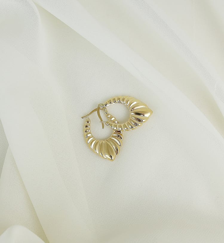 A Pair Of Gold Earrings On A White Fabric