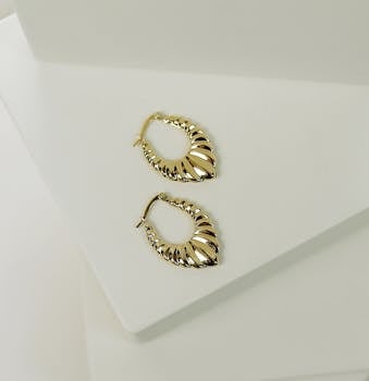Artistic shot of a pair of gold earrings on a textured white surface.