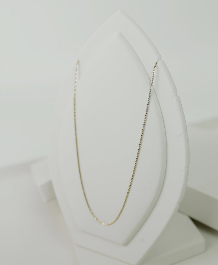 A Gold Necklace On White Necklace Holder
