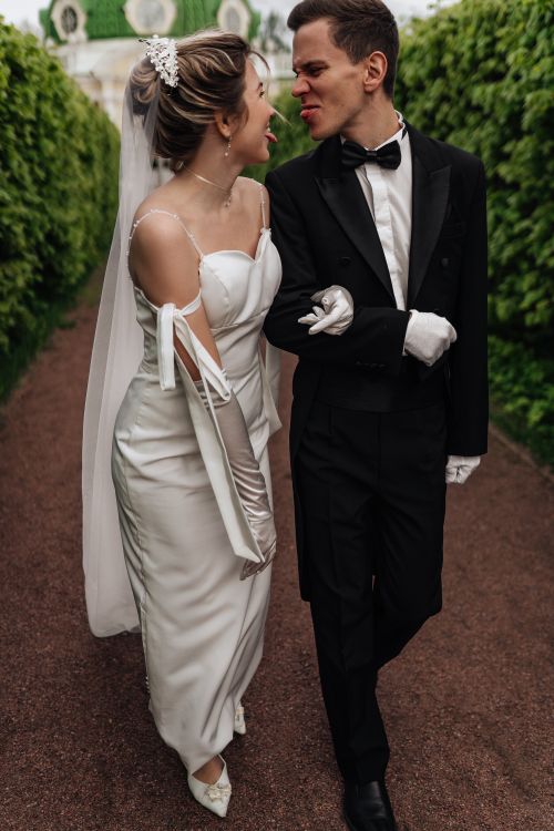 Free Playful bride and groom strolling in a garden, dressed in wedding attire. Stock Photo