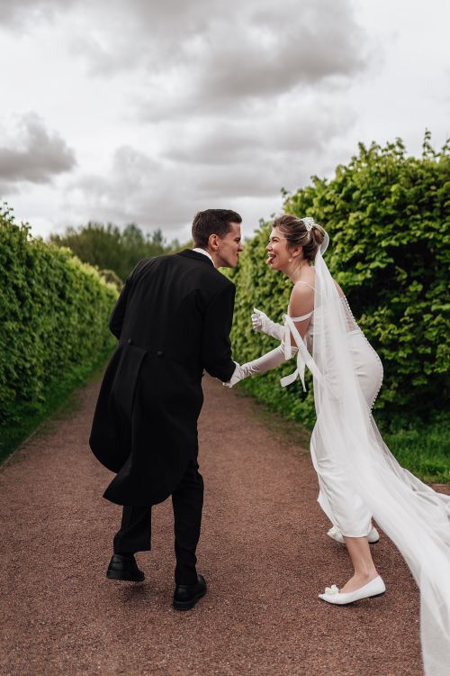 Free Happy bride and groom in a joyful moment on a pathway surrounded by greenery. Stock Photo