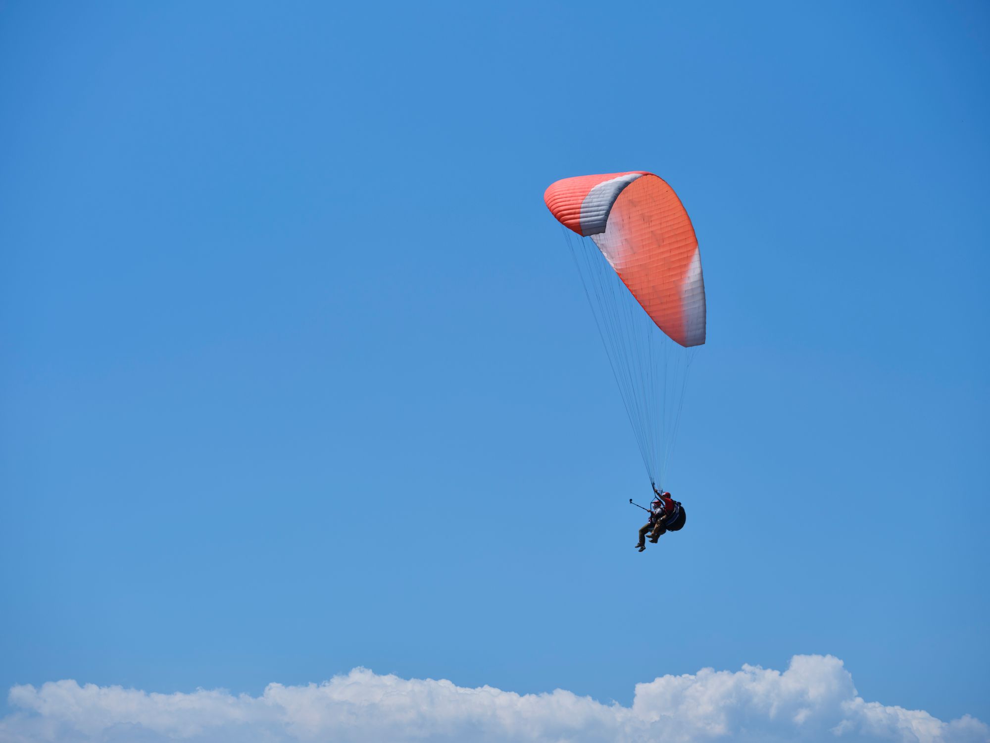 Paraglider soaring with vibrant red parachute against a blue sky Paraglider soaring with vibrant red parachute against a blue sky