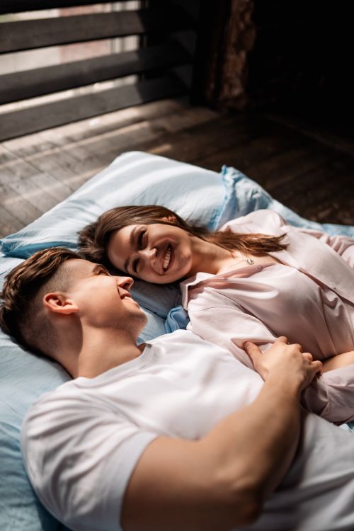 Free Smiling couple lying on a bed sharing happy moments indoors. Stock Photo