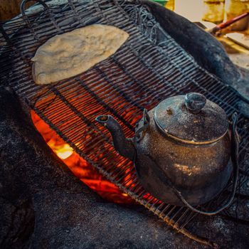 Vintage teapot and flatbread cooking over an open fire grill, embracing rustic charm.