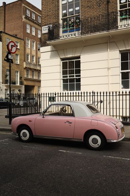 Charming pink vintage car parked by a classic urban building with wrought iron fencing.